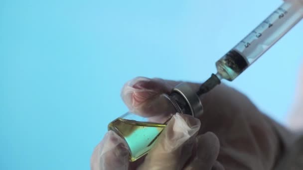 Κοντινό πλάνο των χεριών των γιατρών που ετοιμάζουν ένα εμβόλιο για ένεση σε μπλε φόντο — Αρχείο Βίντεο