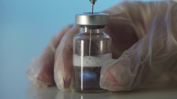 Close-up of the doctors hands holding a syringe with a clear solution and pouring a red substance into an ampoule. The process of developing a vaccine, experimental research in a medical laboratory — Stock Video