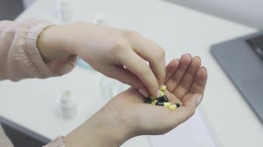 Tanınmayan bir kız elinden hapları alır ve onları suyla temizler, yakın plan.