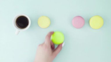 Çok renkli Fransız makarnası kurabiyeleri ve pastel mavi arka planda bir fincan kahve.