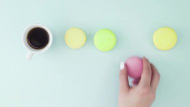 Çok renkli Fransız makarnası kurabiyeleri ve pastel mavi arka planda bir fincan kahve.