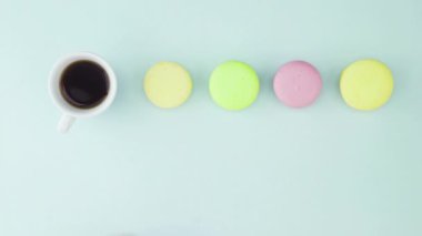 Çok renkli Fransız makarnası kurabiyeleri ve pastel mavi arka planda bir fincan kahve.
