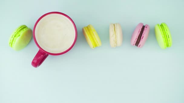 Top view of multicolored French Macarons cookies and a cup of coffee on a pastel blue background — Stock Video