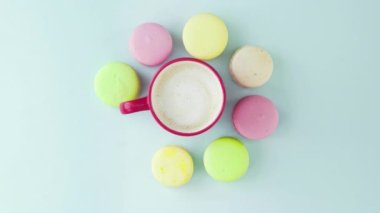 Çok renkli Fransız makarnası kurabiyeleri ve pastel mavi arka planda bir fincan kahve.