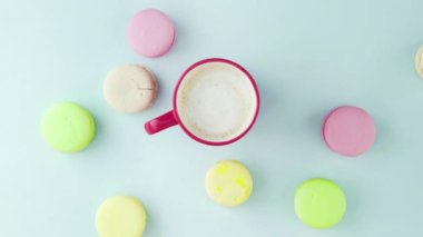 Çok renkli Fransız makarnası kurabiyelerinin üst görüntüsü, bir kadın eli pastel mavi arka plandan bir fincan kahveyi kaldırır