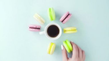 Çok renkli Fransız makarnası kurabiyeleri ve pastel mavi arka planda bir fincan kahve.