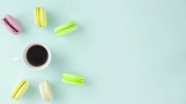 Çok renkli Fransız makarnası kurabiyeleri ve pastel mavi arka planda bir fincan kahve.