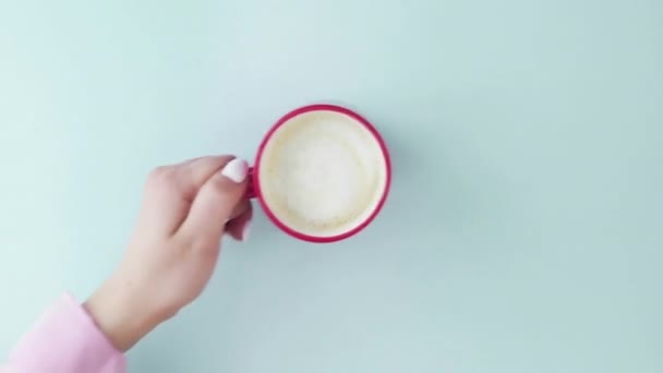 Vista superior de uma xícara de café em um fundo azul pastel. Uma mão de mulher remove uma xícara de café de um fundo azul pastel — Vídeo de Stock