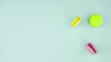 Çok renkli Fransız makarnası kurabiyeleri ve pastel mavi arka planda bir fincan kahve.