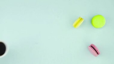 Çok renkli Fransız makarnası kurabiyeleri ve pastel mavi arka planda bir fincan kahve.