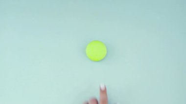 Çok renkli kurabiyelerin üst görüntüsü pastel mavi arka planda Fransız makarnaları. Bir kadının eli kurabiyeyi ortaya taşır..