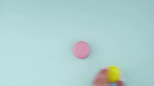 Ovanifrån av flerfärgade franska Macarons cookies på en pastellblå bakgrund. En kvinnlig hand lägger ut kakor — Stockvideo