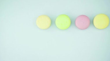Çok renkli Fransız makarnası kurabiyeleri ve pastel mavi arka planda bir fincan kahve.