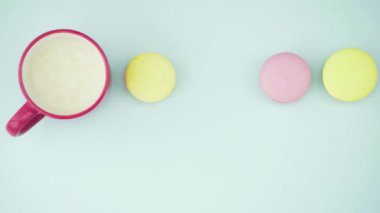 Çok renkli Fransız makarnası kurabiyeleri ve pastel mavi arka planda bir fincan kahve.
