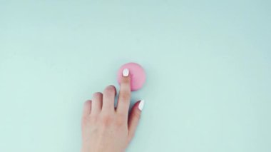 Çok renkli kurabiyelerin üst görüntüsü pastel mavi arka planda Fransız makarnaları. Bir kadının eli kurabiyeyi ortaya taşır..