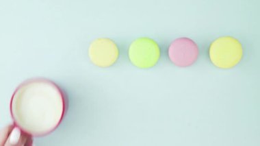 Çok renkli Fransız makarnası kurabiyeleri ve pastel mavi arka planda bir fincan kahve.