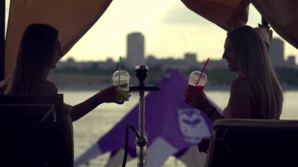 Twee jonge vrouwen op het strand zonnebaden, hookah roken en cocktails drinken — Stockvideo