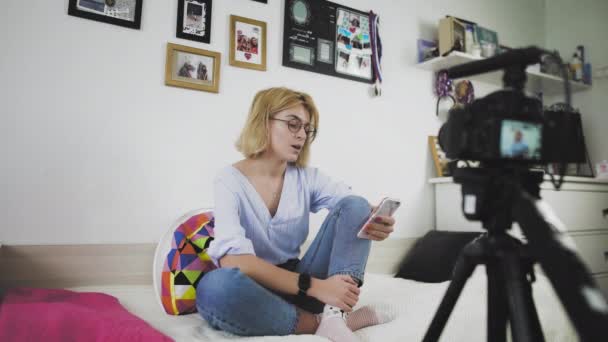 Na gauči sedí mladá žena s brýlemi a usmívá se a mluví do kamery. — Stock video