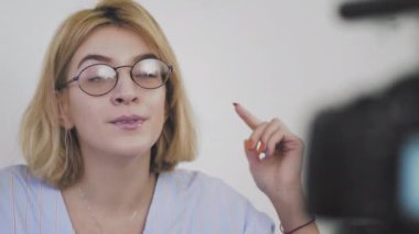 Kanepede oturan, gülümseyen ve kamerayla konuşan gözlüklü genç bir kadının yakın çekimi. Abonelerine veda ediyor.