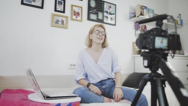 Na pohovce sedí mladá žena s brýlemi, usmívá se a mluví do kamery. Rozloučí se se svými předplatiteli — Stock video