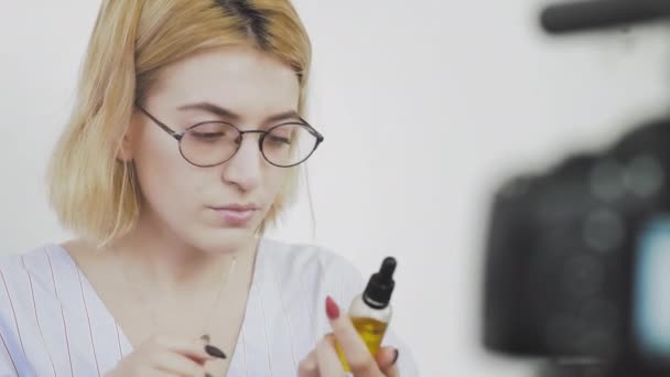 안경을 쓴 젊은 여성이 웃으며 카메라 앞에서 새 제품에 대해 이야기하는 모습. 자기 관리를 위한 화장품의 검토 — 비디오