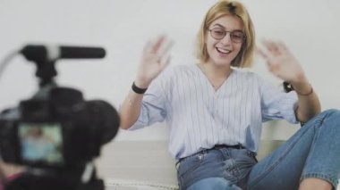 Gözlüklü genç bir kadın kanepede oturuyor, gülümsüyor ve kameraya konuşuyor. Abonelerine veda ediyor.