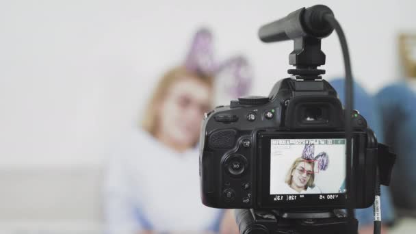 Молода жінка в окулярах сидить на дивані посміхаючись, розмовляючи з камерою — стокове відео