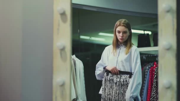 Een mooi meisje past kleren in de paskamer in een kledingwinkel. Winkelen — Stockvideo