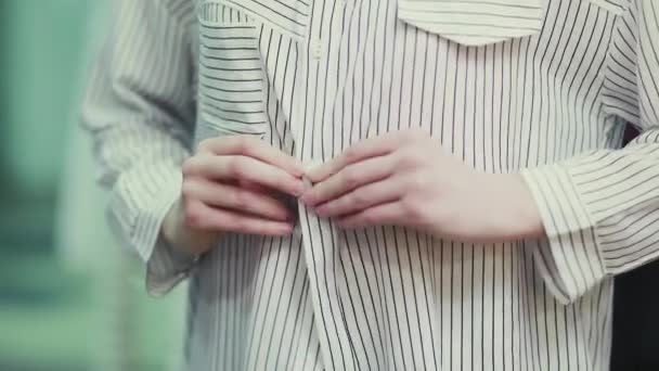 Les mains des femmes boutonnent les boutons sur un chemisier rayé, gros plan — Video