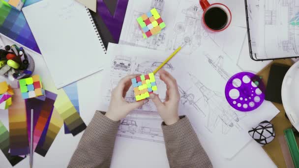 Vista superior de las manos de una diseñadora femenina resolver un rompecabezas con un cubo Rubiks. Cubo rompecabezas, un juego de puzzle. — Vídeo de stock
