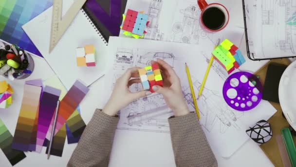 Bovenaanzicht van de handen van een vrouwelijke ontwerper los een puzzel op met een Rubiks kubus. Kubus puzzel, een puzzel spel. — Stockvideo