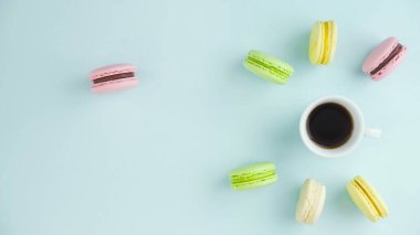 Çok renkli Fransız makarnası kurabiyeleri ve pastel mavi arka planda bir fincan kahve.