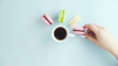 Çok renkli Fransız makarnası kurabiyeleri ve pastel mavi arka planda bir fincan kahve.