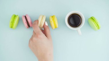 Çok renkli Fransız makarnası kurabiyeleri ve pastel mavi arka planda bir fincan kahve.