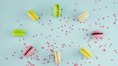 Çok renkli kurabiyelerin üst görüntüsü pastel mavi bir zemin üzerinde güzel dağınık konfetiyle Fransız Makarnaları