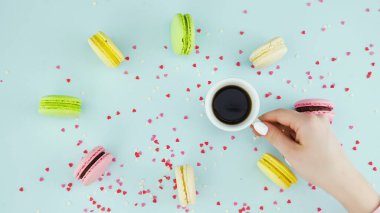 Renkli kurabiyeler, Fransız makarnaları ve pastel mavisi arka planda güzel dağınık konfetiyle bir fincan kahve.