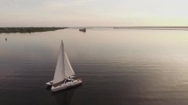 Küçük bir yelkenli yat gün batımında nehirde yelken açar.