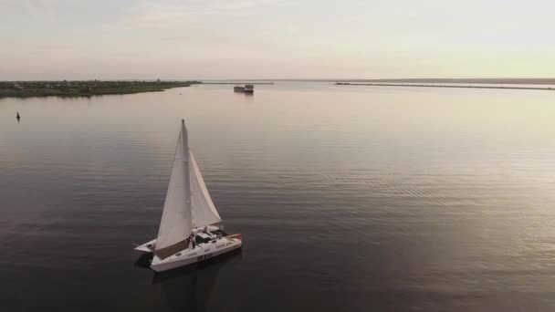 Eine kleine Segeljacht segelt bei Sonnenuntergang auf dem Fluss — Stockvideo