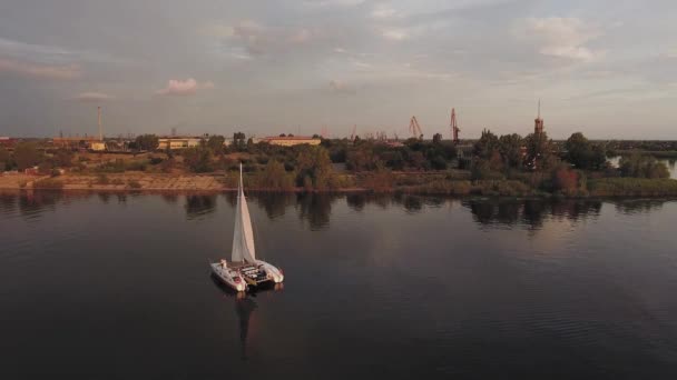 Küçük bir yelkenli yat gün batımında nehirde yelken açar. — Stok video