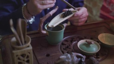 Çay dükkanındaki genç bir adam ahşap bir spatulaya çay yaprakları koyar.