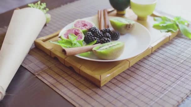Смачна фруктова страва на тарілці з запашним зеленим чаєм на дерев'яному підносі — стокове відео