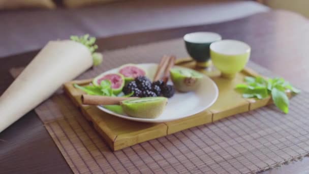 Вкусное фруктовое блюдо на тарелке с ароматным зеленым чаем на деревянном подносе — стоковое видео