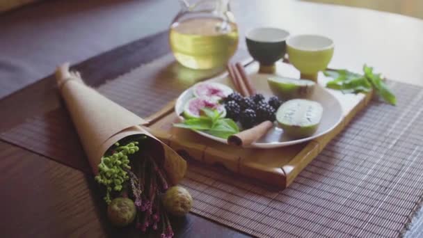 Pyszne danie owocowe na talerzu z pachnącą zieloną herbatą na drewnianej tacy — Wideo stockowe
