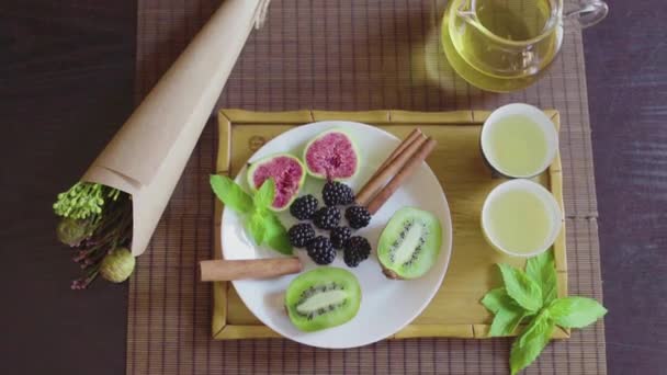Délicieux plat de fruits sur une assiette avec thé vert parfumé sur un plateau en bois — Video