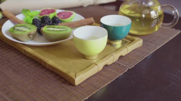 Delicioso plato de frutas en un plato con té verde fragante en una bandeja de madera — Vídeo de stock