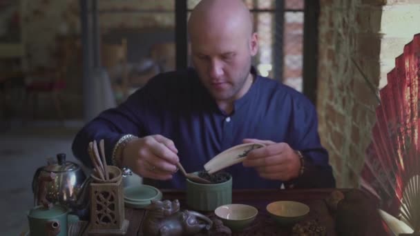Un joven en una tienda de té pone hojas de té en una cuchara de madera con una espátula de madera — Vídeo de stock