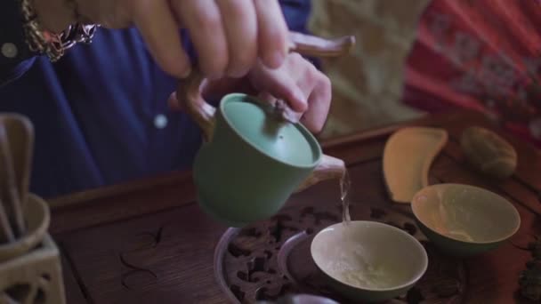 Мужчина наливает чай в чайные чашки на деревянный поднос в чайной комнате — стоковое видео