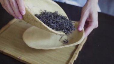 Kadınların elleri, çay yapraklarını ahşap bir kaseden masanın üzerindeki çay odasına taşır.