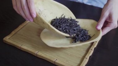 Kadınların elleri, çay yapraklarını ahşap bir kaseden masanın üzerindeki çay odasına taşır.