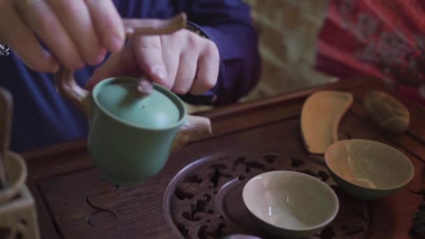 Um homem derrama chá em copos de chá em uma bandeja de madeira em uma sala de chá — Vídeo de Stock